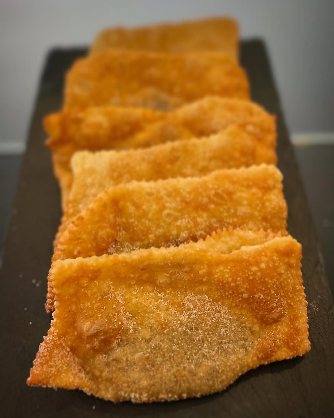 Fila de pastéis fritos dourados numa travessa de ardósia