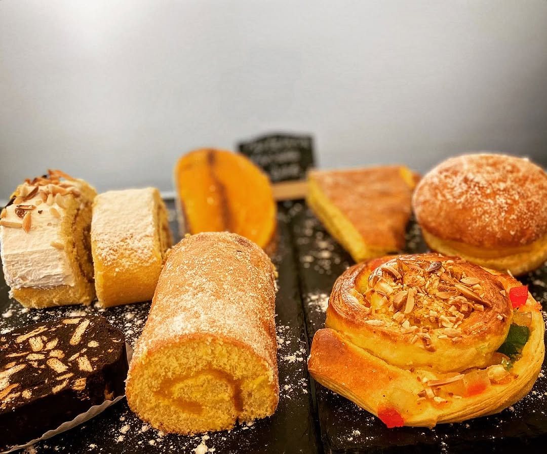 Seleção de bolos e pastelaria numa bancada, com rolos, bolo de chocolate e doces com amêndoa