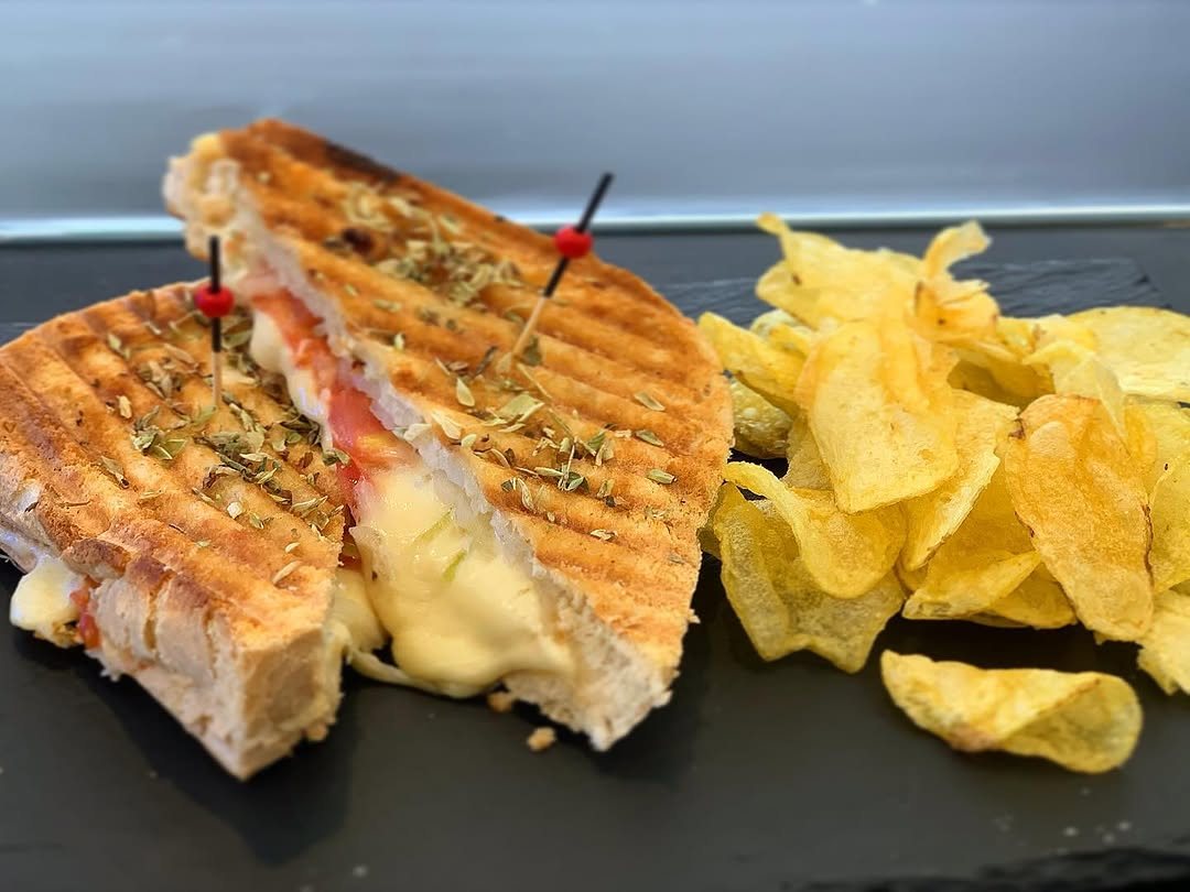 Tosta grelhada cortada ao meio, com queijo derretido, ao lado de batatas fritas, numa travessa escura